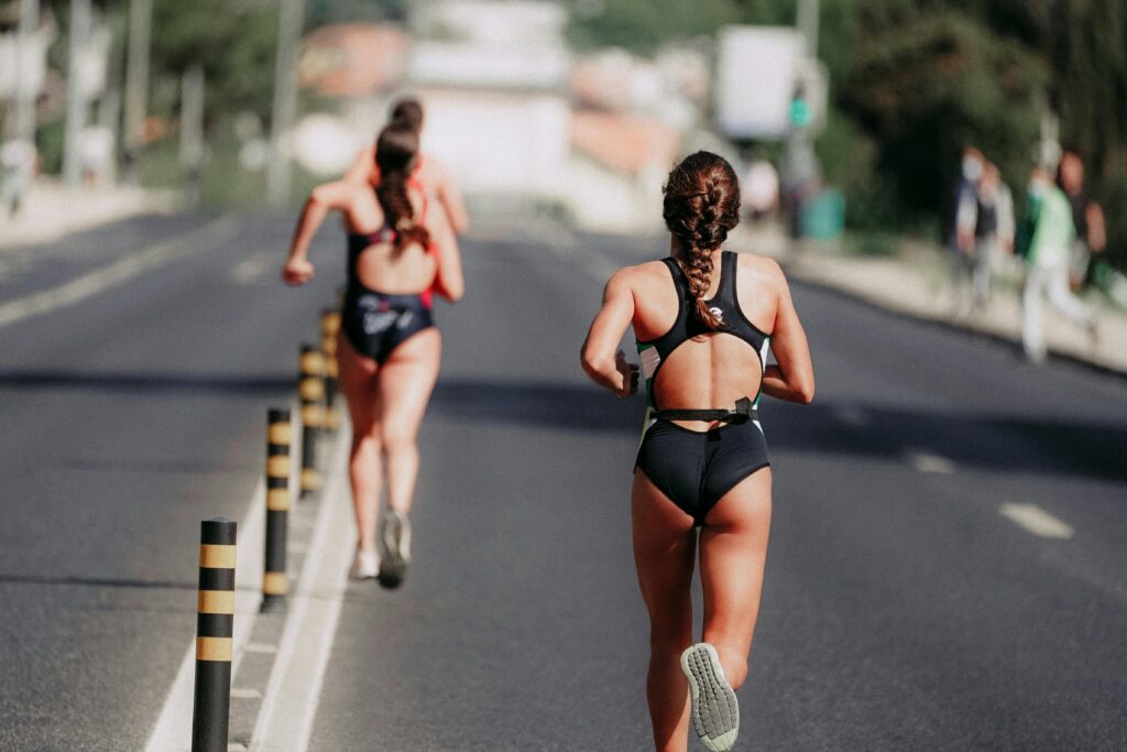 Two women athletes running on an open road during a marathon event, showcasing endurance and determination.